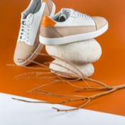 picture of a white and beige pair of shoes on top of two rounded rocks in a dark orange background