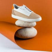 picture of a white and beige shoe on top of two rounded rocks in a dark orange background half folded